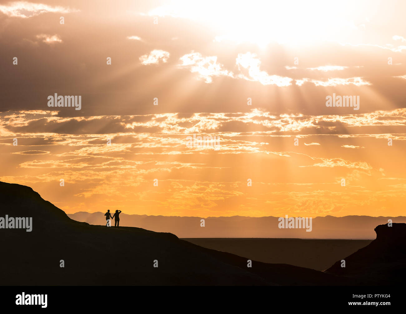 Romantic Couple holding hands, romance Sunset with sun ray burst over flaming cliffs in Mongolia Stock Photo