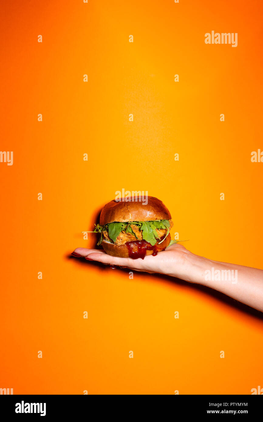Hand holding chicken burger against orange background. Stock Photo