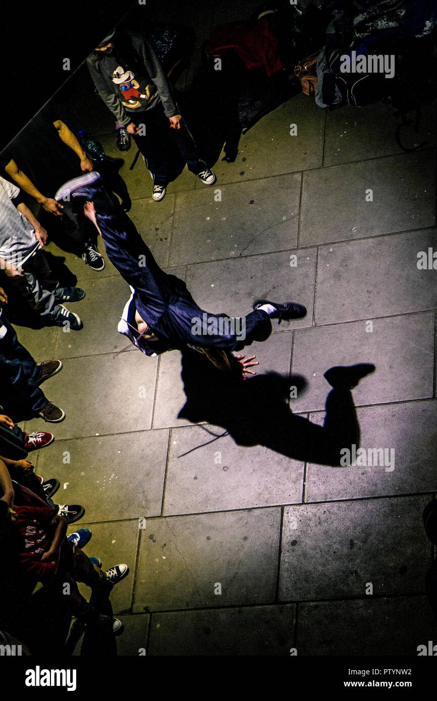 Breakdancer performing acrobatic dance moves at night as other teenagers watch, photographed from above on London's South Bank Stock Photo
