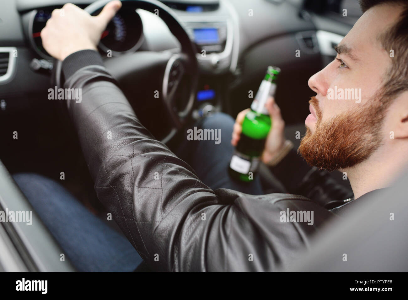 Drunk young man with a beard with a bottle of beer in his hand behind ...