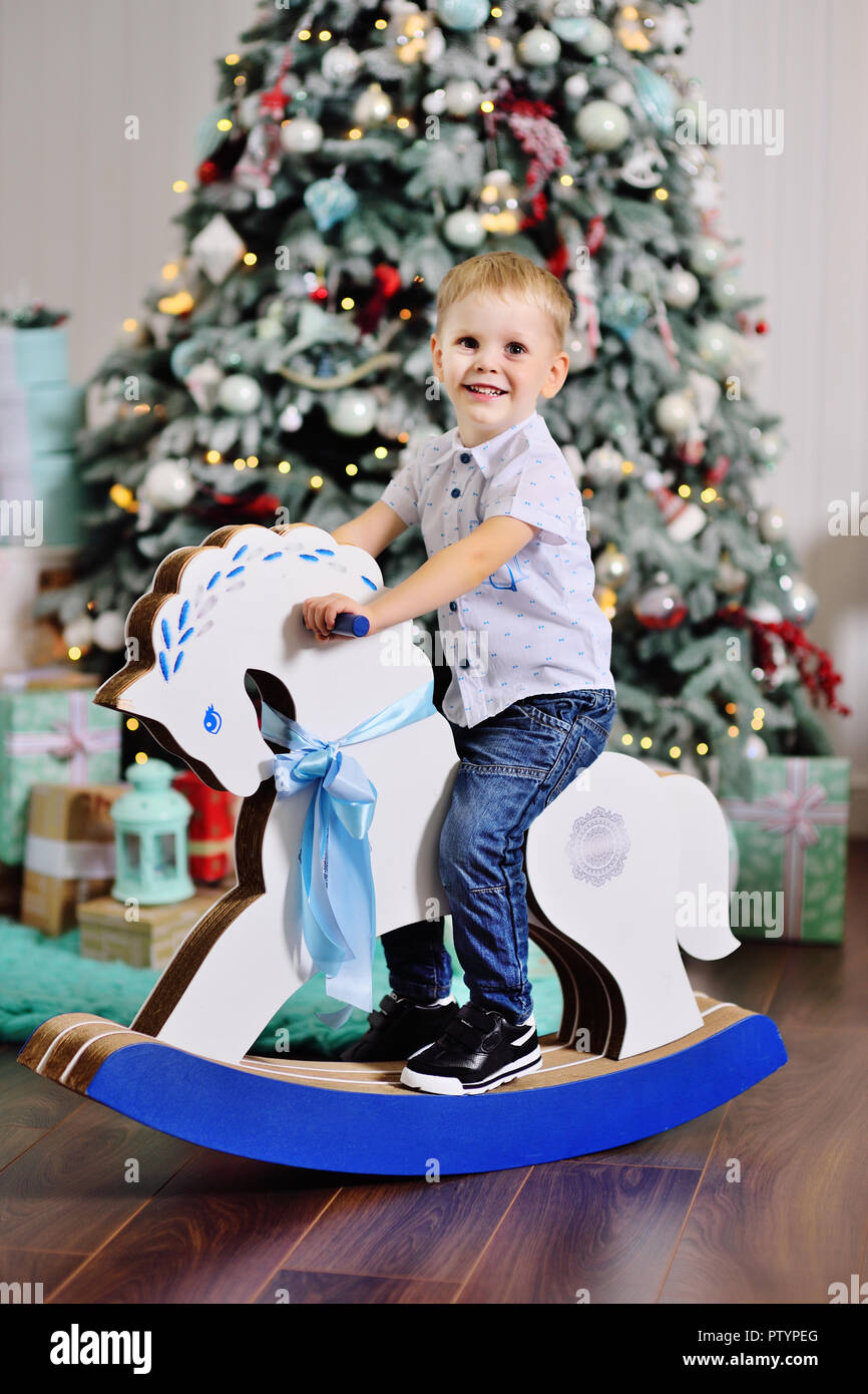 cute baby boy on a toy horse against the background of a Christmas tree Stock Photo