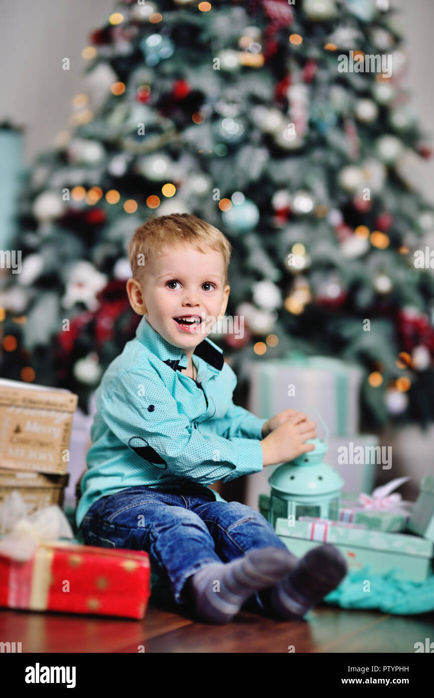 baby boy opens boxes with gifts under the Christmas tree and smiles ...