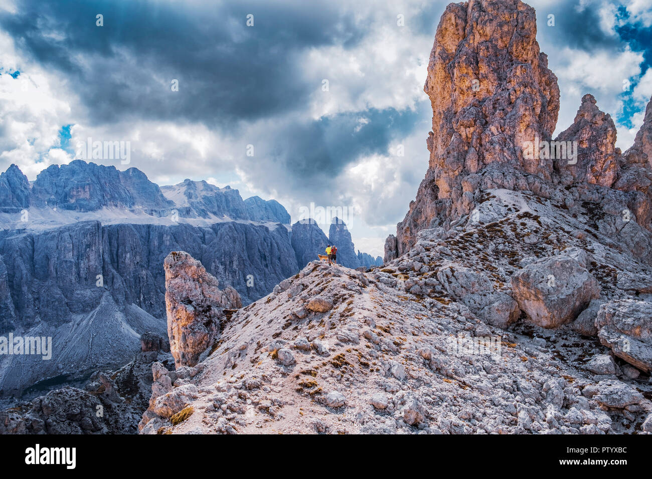 View from Puez-Geisler reserve in the Dolomite alps. Hiker with dogs standing on the rim, viewing the mountains. Stock Photo