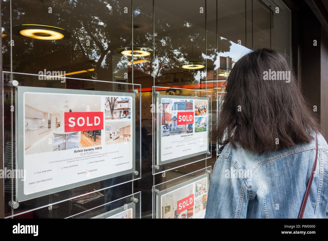 A young woman looking into an estate agents window trying to get on the property ladder, Barnes, London, UK Stock Photo