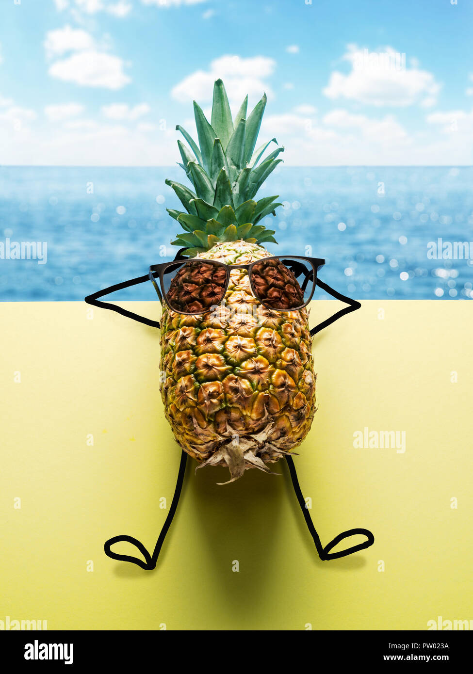 Pineapple man in sun glasses on blue-and-yellow background. Sea and cloudly sky at the background. Stock Photo