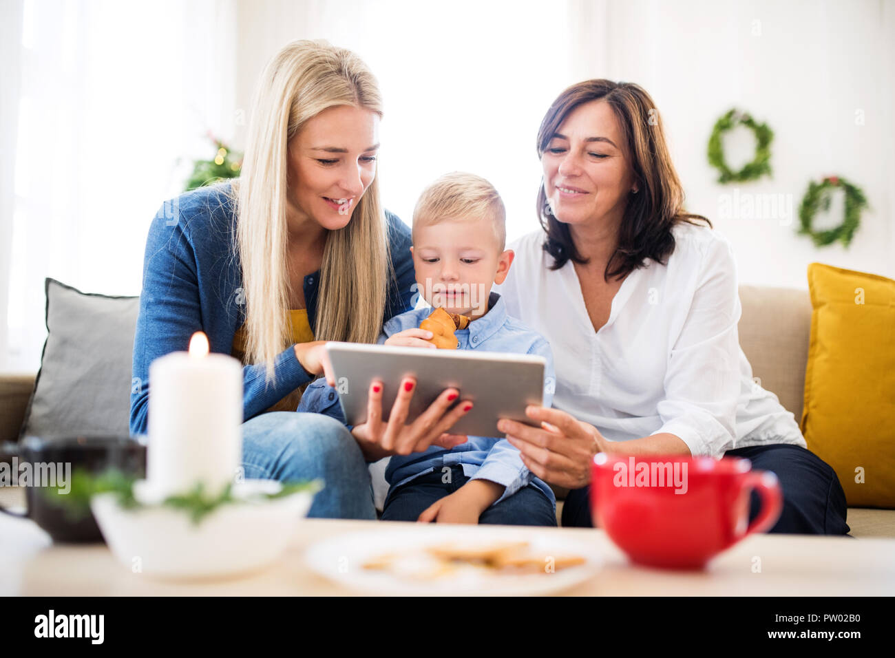 A small boy with mother and grandmother at home at Christmas time, using tablet. Stock Photo