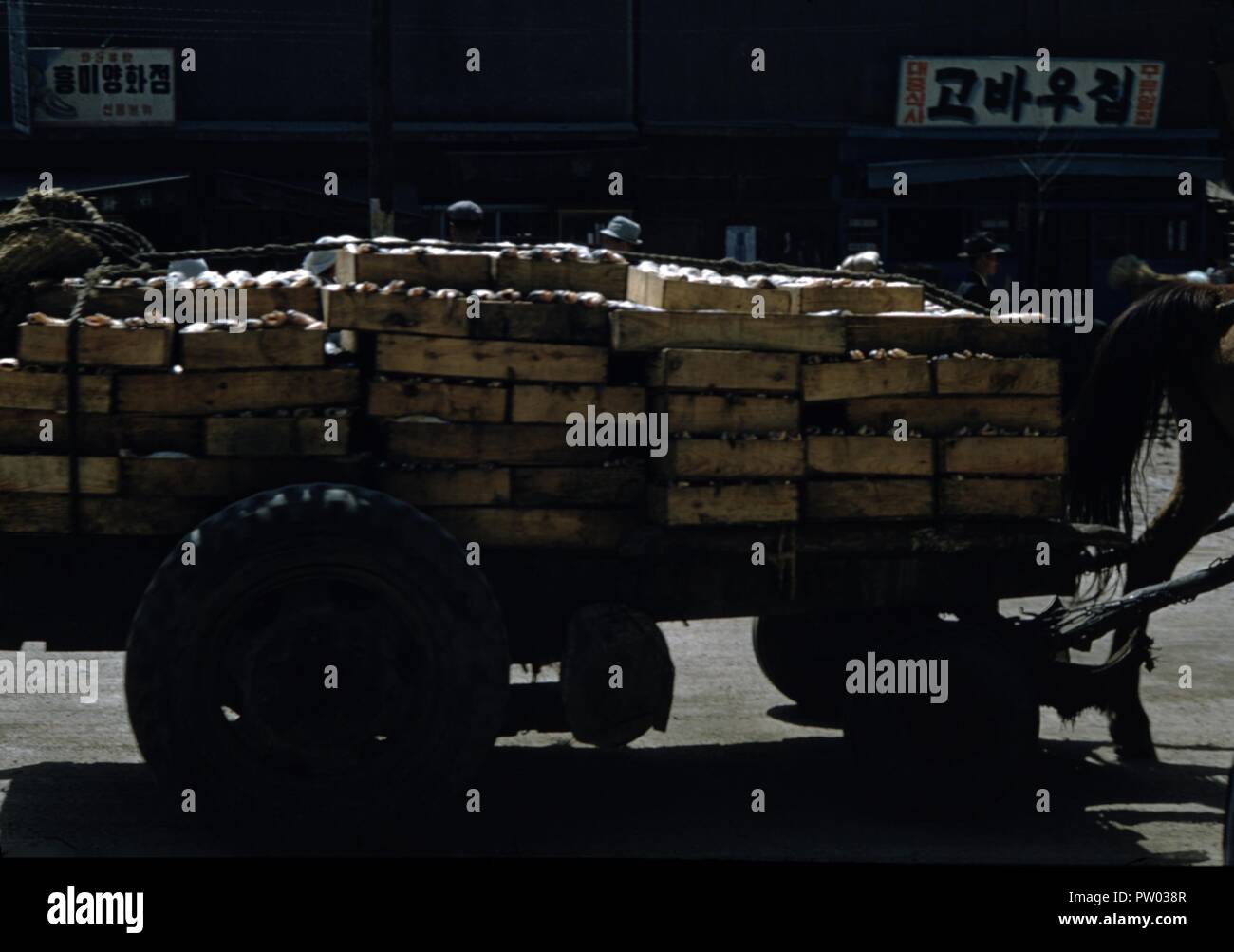 Color photograph of a horse cart (with the horse's tail and rear leg visible at right) loaded with low crates that appear to contain vegetables such as gourds, with signs written with Japanese characters visible in the background, likely photographed in Japan during the mid-twentieth century, 1965. () Stock Photo