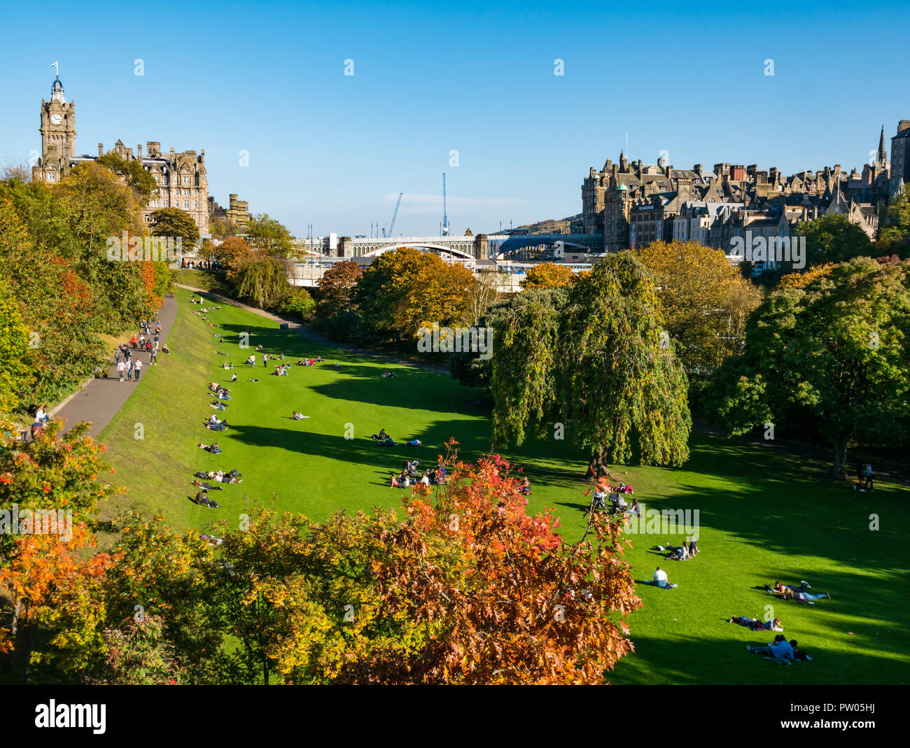 People sitting in Princes Street Gardens in Autumn sun with Balmoral Hotel clock tower and North Bridge, Edinburgh, Scotland, UK Stock Photo