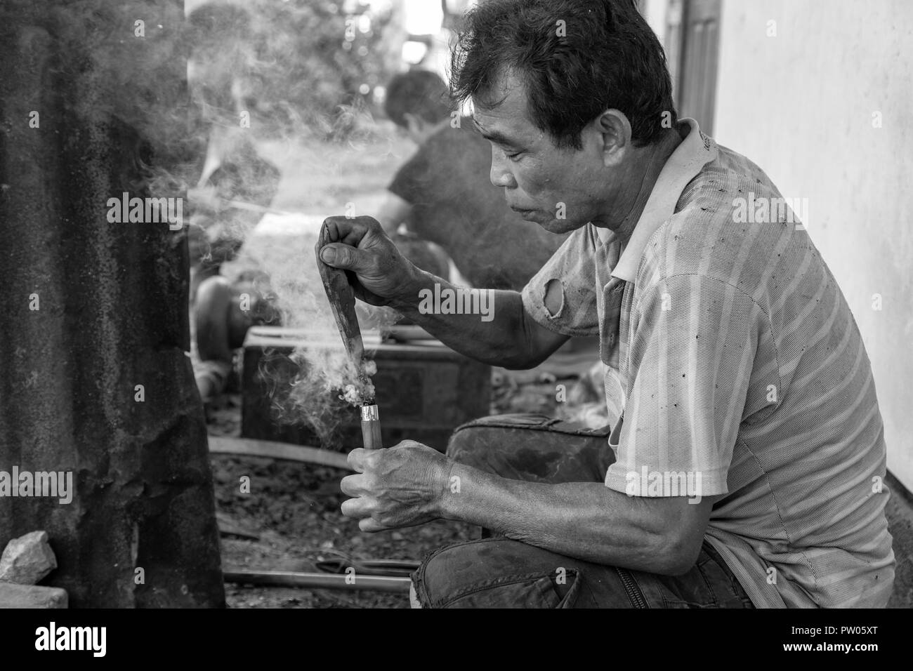 LUANG PRABANG, LAOS - OCTOBER 8: An unidentified man burns a hot knife tang into a handle at a local village forge in Luang Prabang, Laos on October 8 Stock Photo