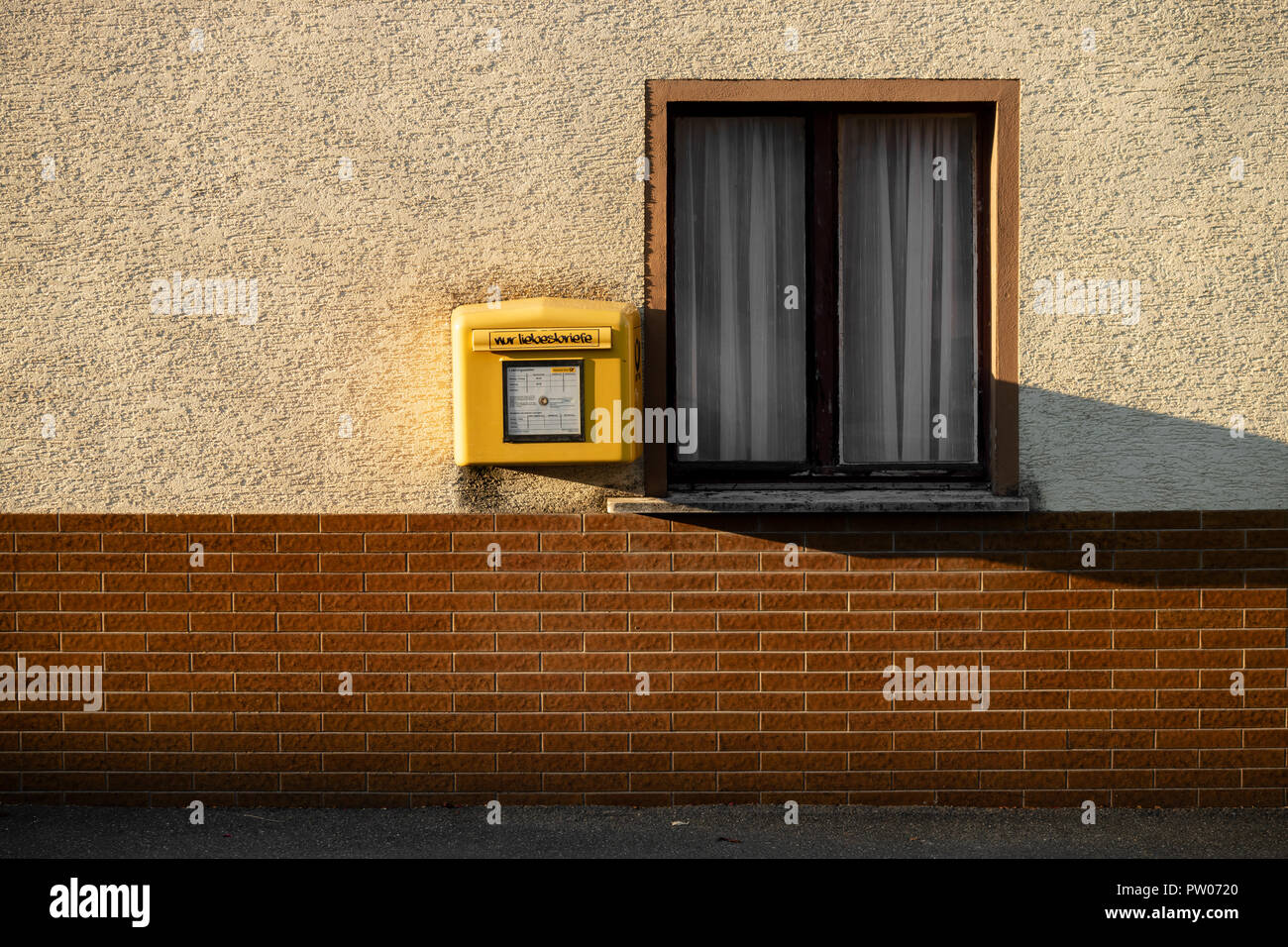 Standard yellow letterbox of German Postal Service hanging on a wall next to a window Stock Photo