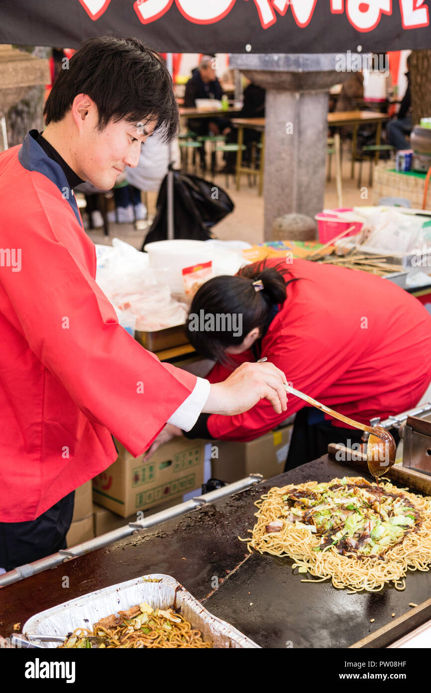 Japanese man in traditional red happi jacket, at Yakisoba takeaway stall cooking fried buckwheat