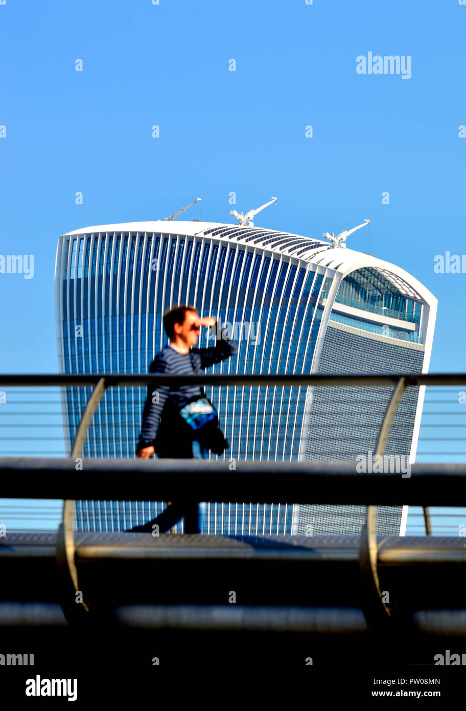 Man (out of focus) walking across the Millennium Bridge with the Walkie Talkie Building (20 Fenchurch Street) in focus behind, London, England, UK. Stock Photo