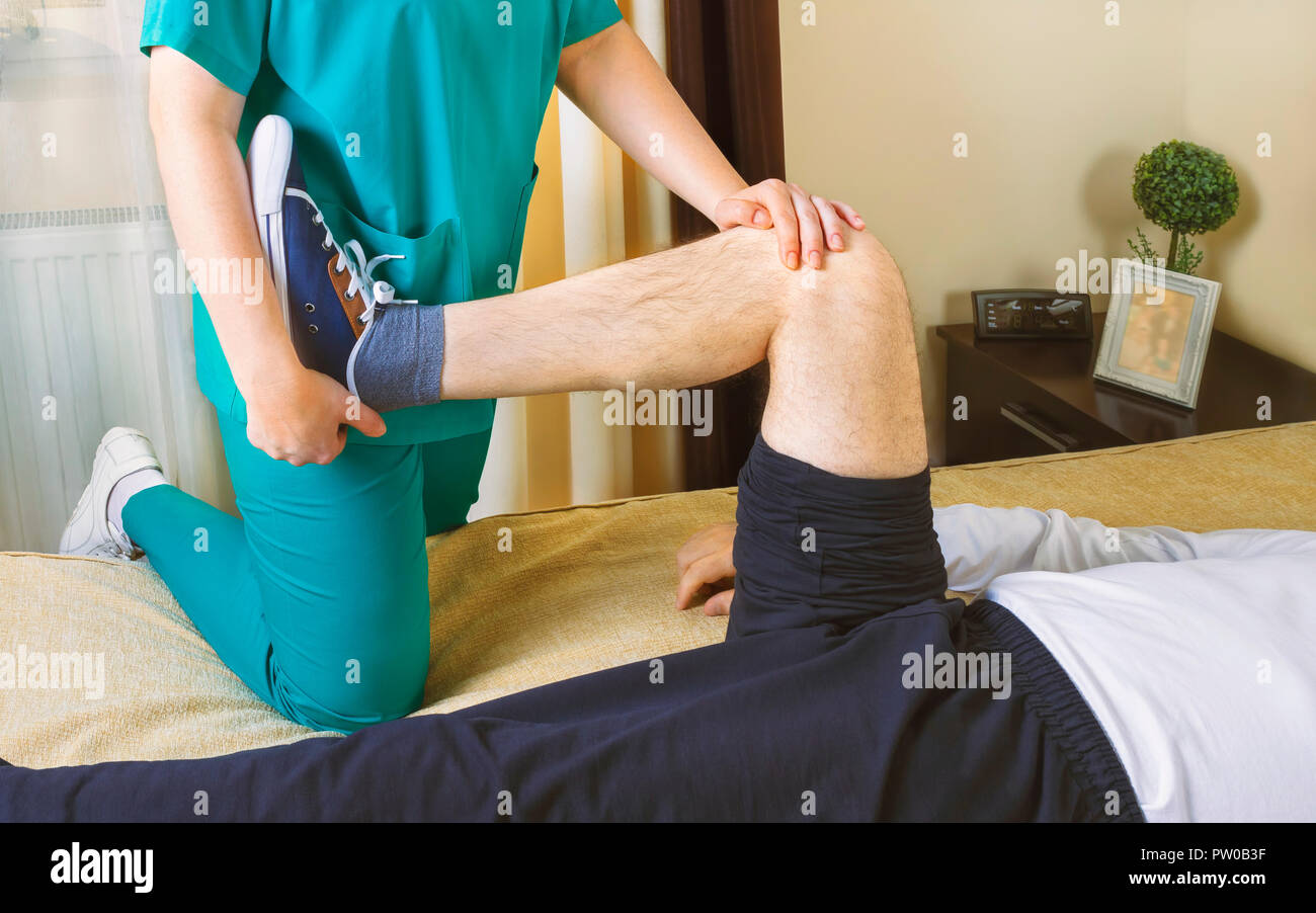 Physiotherapist doing exercises for leg recovery to immobilized male patient at home. People, health and recovery concept. Stock Photo