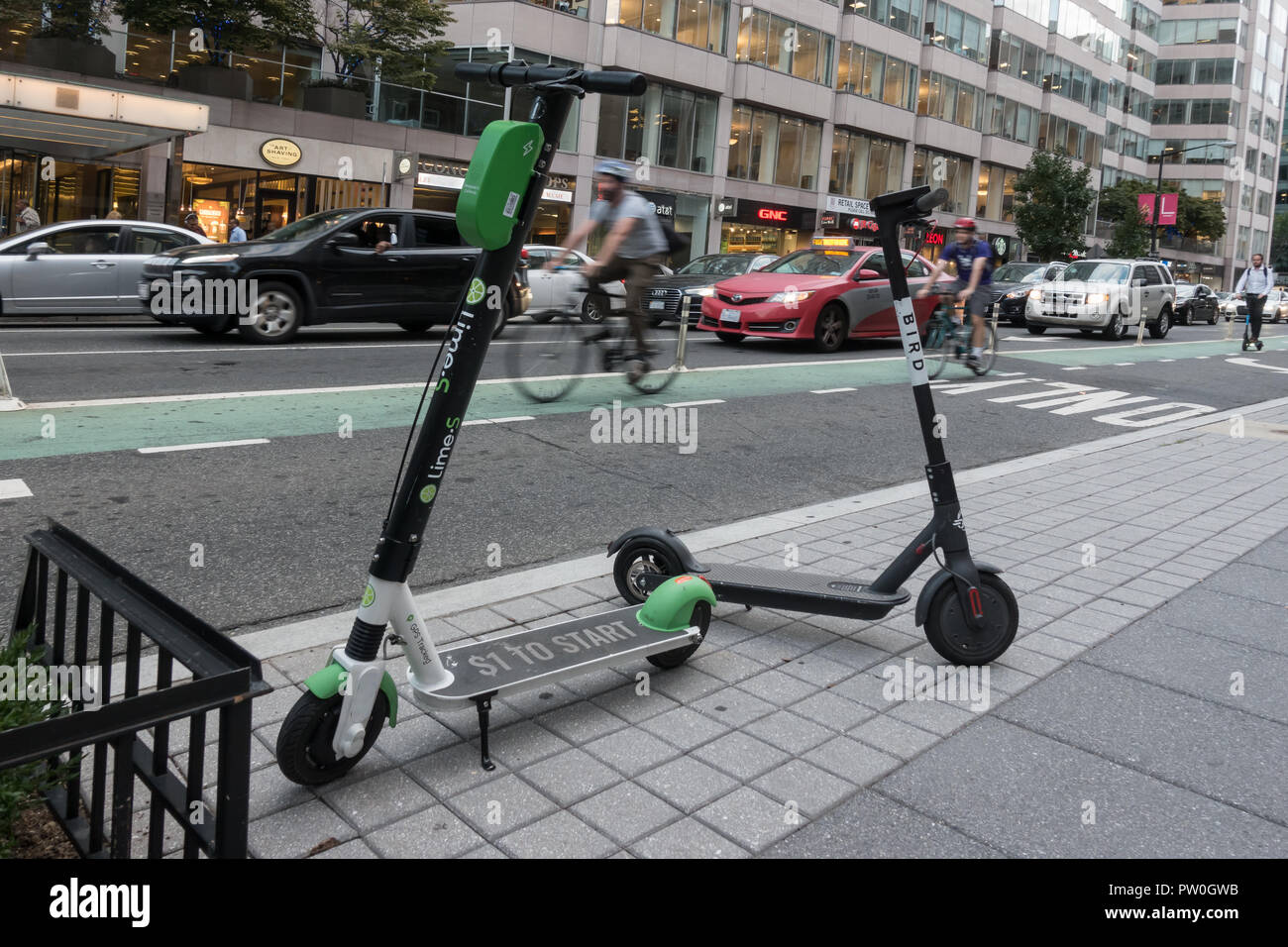 Bike rider in bike lane, two dockless electric scooters parked, downtown, Washington, DC. Lime-S and Bird scooters among several operating in DC Stock Photo