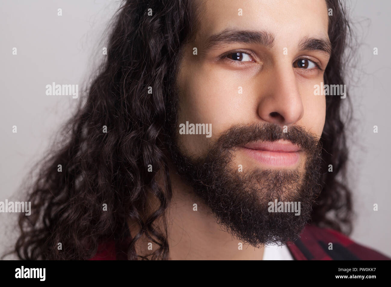 Closeup portrait of handsome confident man with black long curly hair and beard, looking at camera and smiling. male healthcare and beauty concept. in Stock Photo