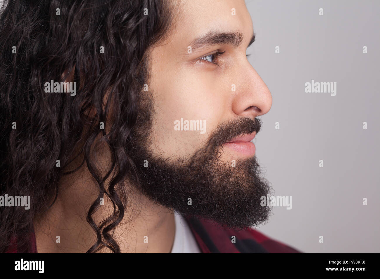 Closeup profile side view of handsome confident man with black long curly hair and beard, looking away with smile. male healthcare and beauty concept. Stock Photo