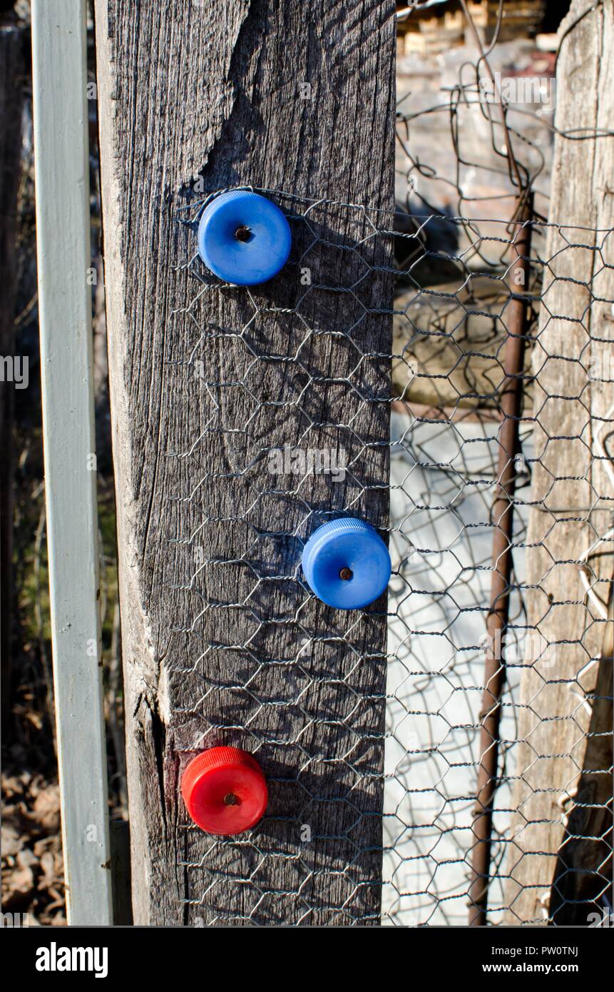 detail of unusual use of plastic bottle cups on old wooden gate with  wires on sunny day Stock Photo