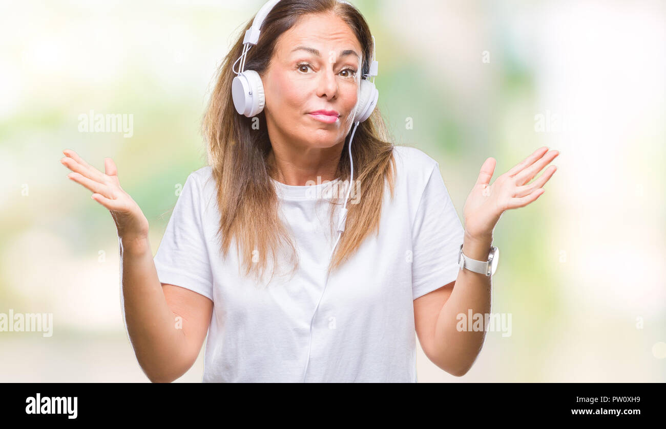 Middle age hispanic woman listening to music wearing headphones over ...