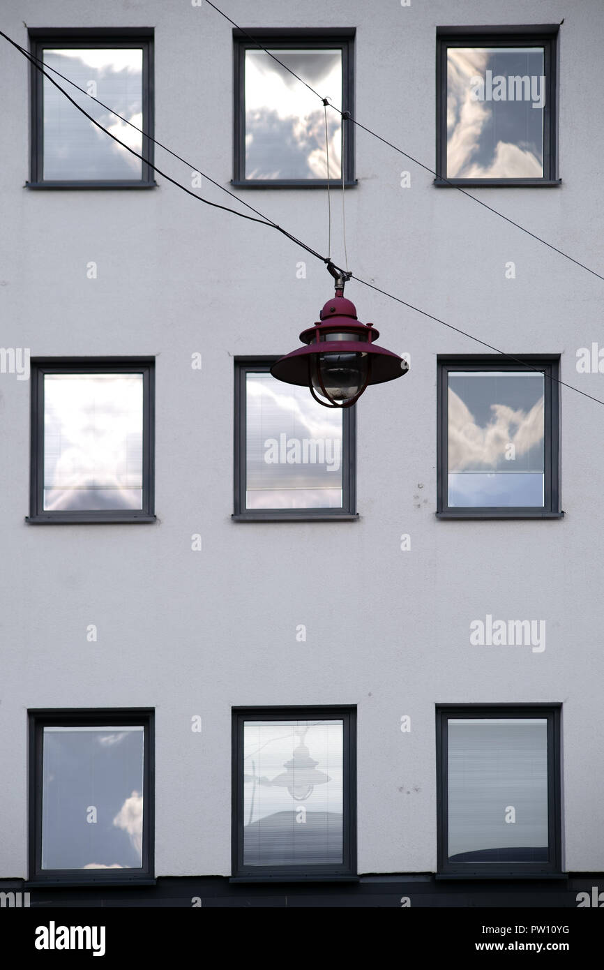 A hanging lamp in front of the facade of a residential building with windows in which the clouds are reflected. Stock Photo