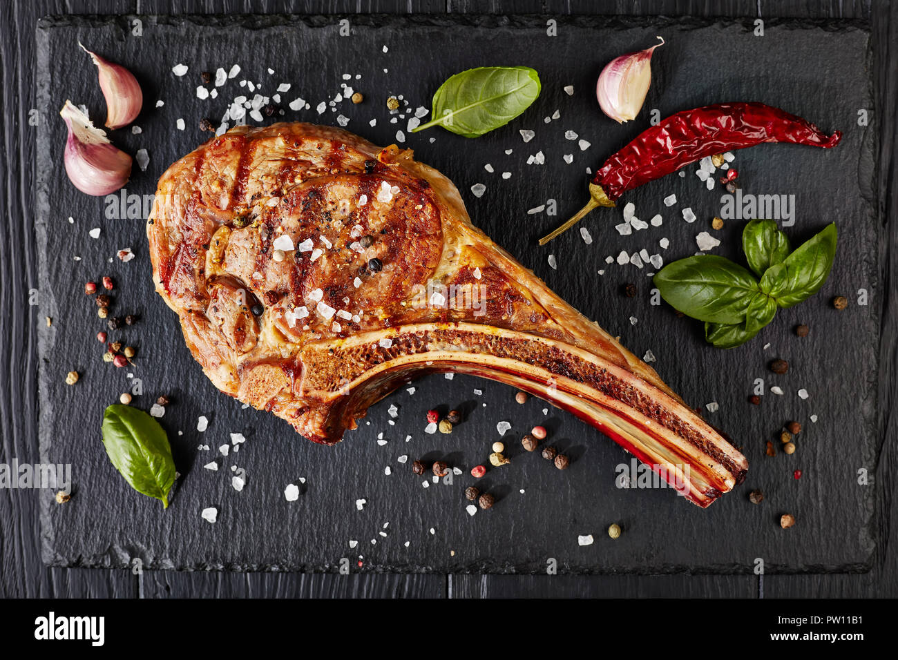 close-up of grilled tomahawk steak or cowboy beef steak on a black slate board with garlic, fresh basil, view from above, flat lay Stock Photo