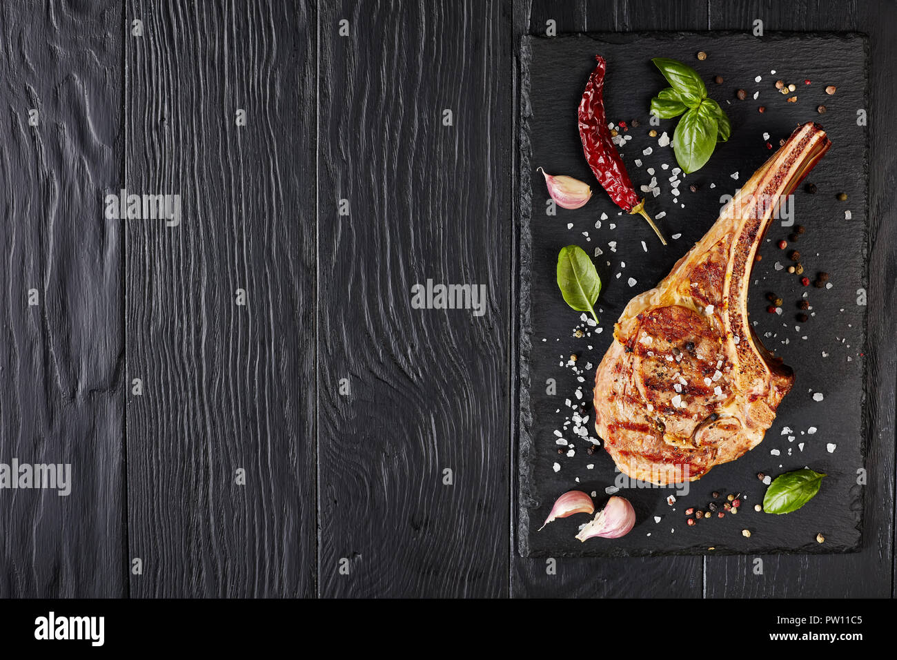 roasted tomahawk steak or cowboy beef steak on a black slate board with garlic, fresh basil, view from above, flat lay Stock Photo