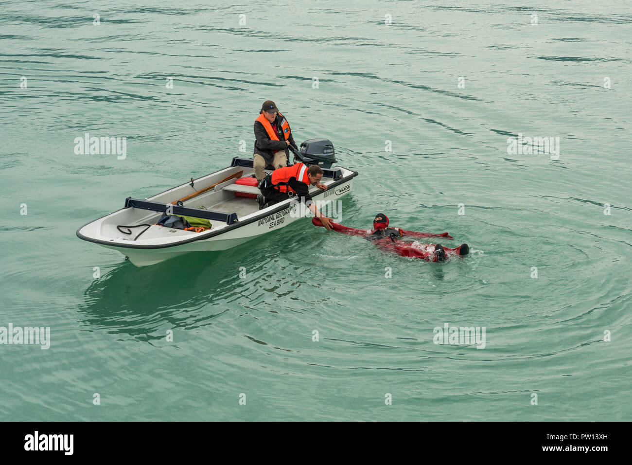 Ship crew member in the water dressed in a survival suit is helped by crew members in a Boston Whaler boat during Man Overboard drill on the Lindblad  Stock Photo