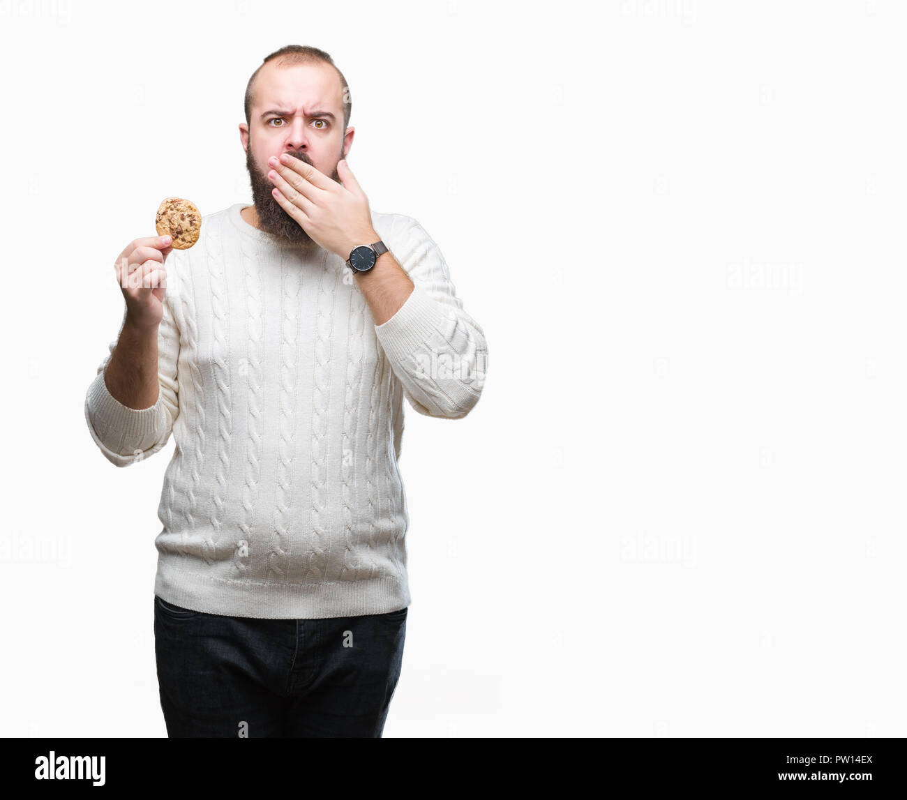 Young hipster man eating chocolate chips cookie over isolated background cover mouth with hand shocked with shame for mistake, expression of fear, sca Stock Photo