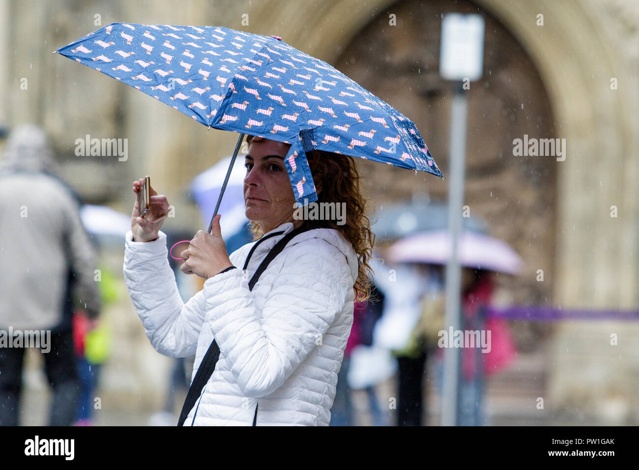 Bath, UK. 12th October, 2018. A woman is pictured a she takes a photograph in front of Bath Abbey as heavy rain showers make their way across the UK. Credit: Lynchpics/Alamy Live News Stock Photo