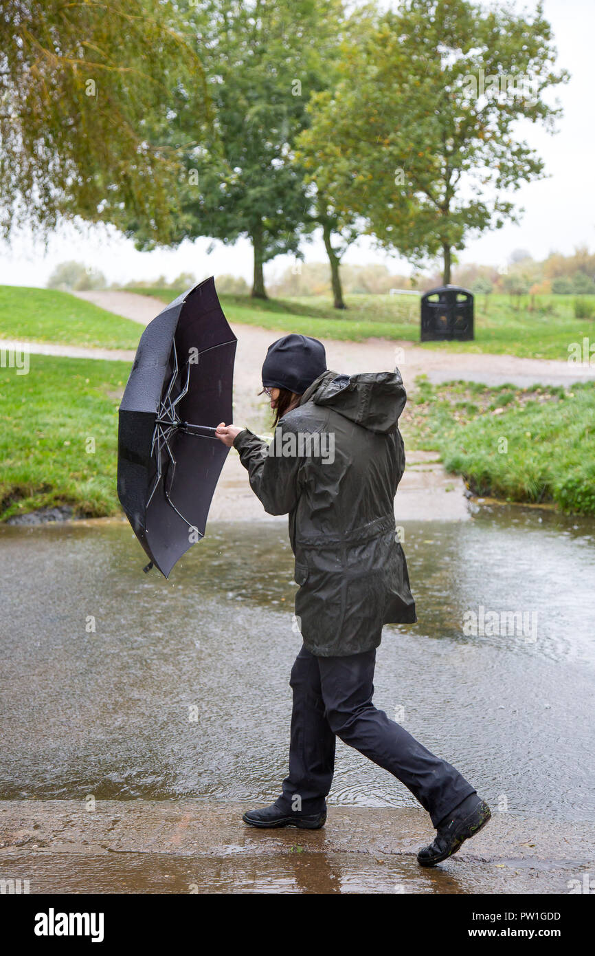 Kidderminster, UK. 12th October, 2018. UK weather: it's very wet and very windy! Milder temperatures may be tempting us outdoors, but visitors to a local park in Kidderminster have to brave heavy spells of rain and increasingly strong, gusting winds this morning. A drenched lady, in wet rain coat, is isolated here struggling in the windy weather with her umbrella. Credit: Lee Hudson/Alamy Live News Stock Photo