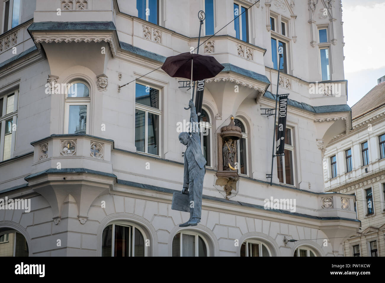 Sculpture of a man hanging from an umbrella on a telephone wire in
