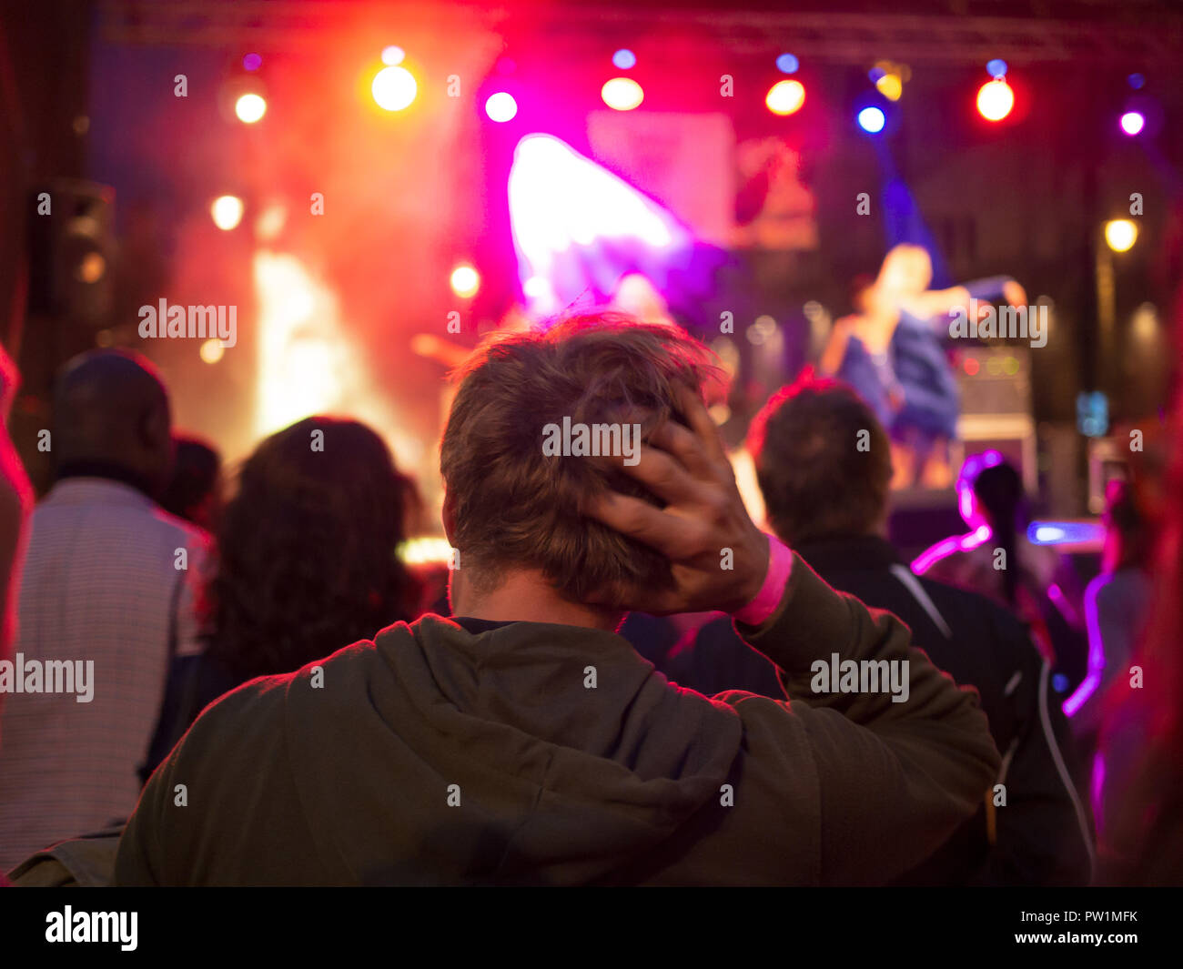Lonely sad young man in the crowd watching a concert, hand on head. Stock Photo