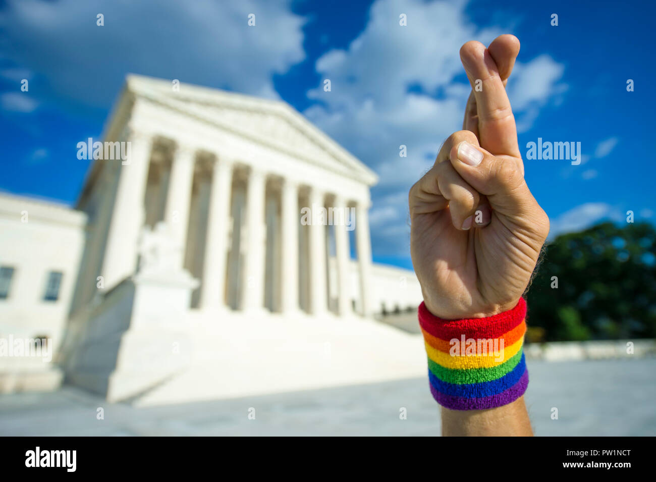 Hopeful hand wearing gay pride rainbow flag wristband crossing fingers for good luck outside the Supreme Court building in Washington, DC, USA Stock Photo