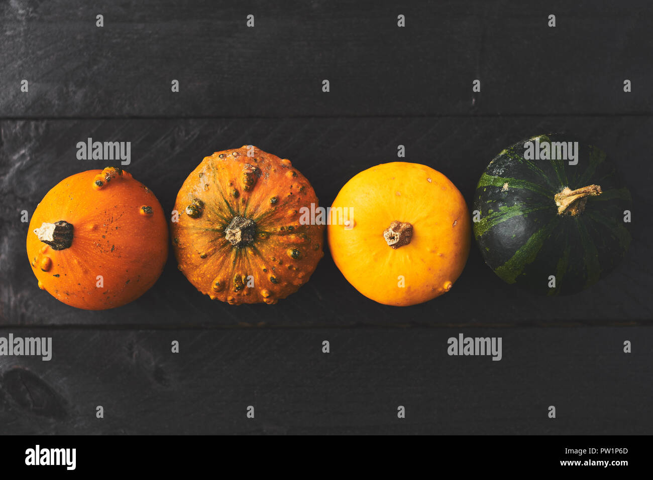 Simple autumn background with yellow, orange and green pumpkins on black wood with copy space. Top view. Stock Photo