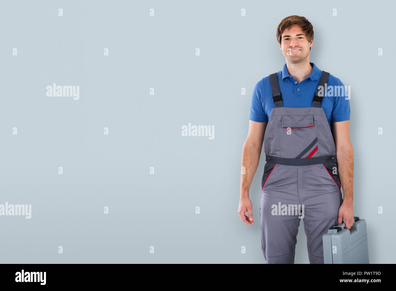 Portrait Of A Happy Male Technician Holding Toolbox On Gray Background Stock Photo