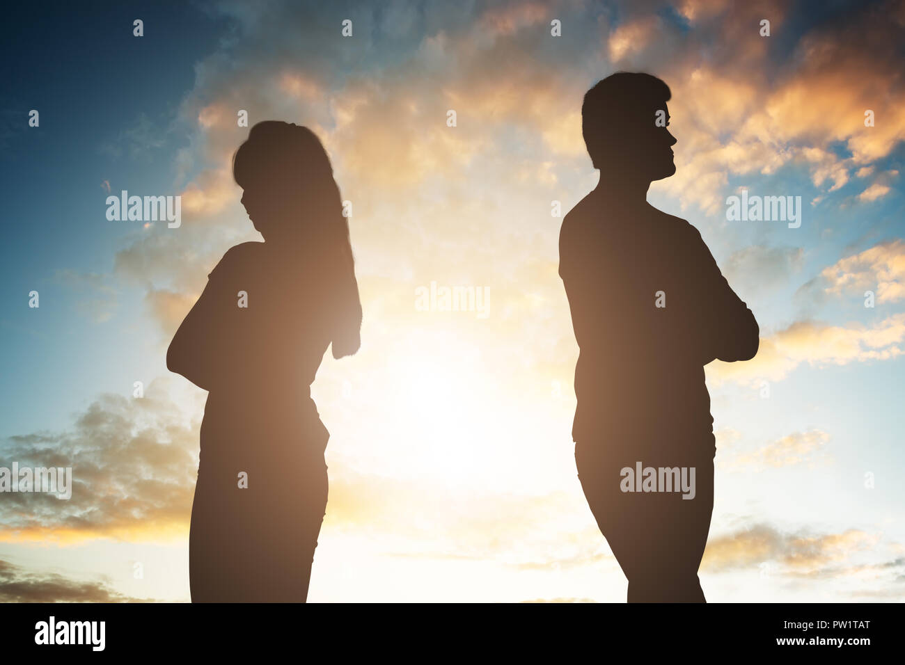 Silhouette Of A Unhappy Couple Standing Back To Back Against Cloudy Sky At Sunset Stock Photo
