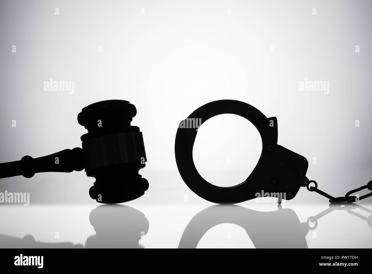 Silhouette Of Handcuff Near Gavel With Sounding Block On Reflective Background Stock Photo