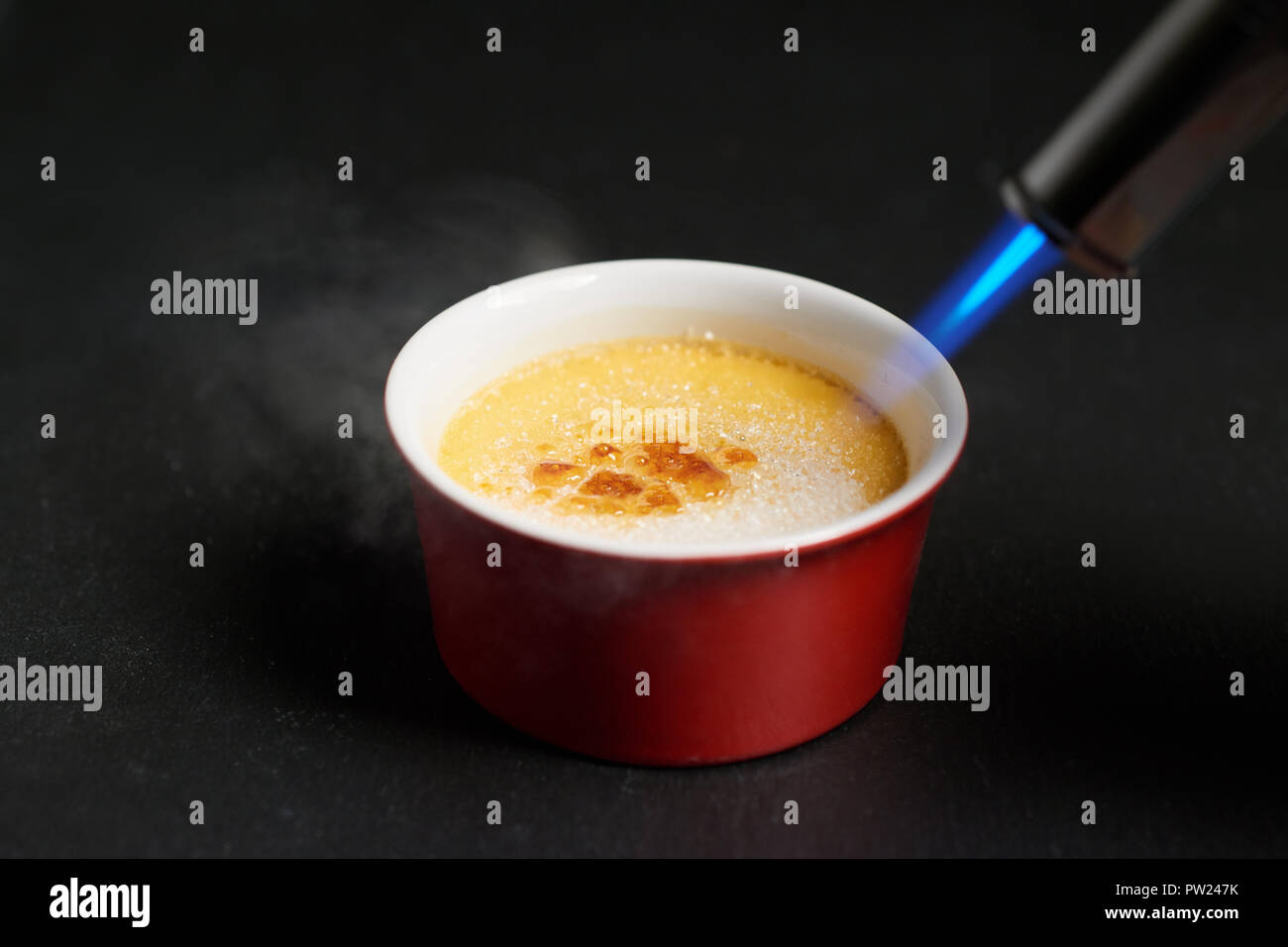 Caramelising sugar on top of creme brulee with flaming torch on dark