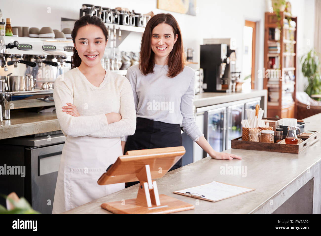 Two female coffee shop owners smiling behind counter Stock Photo - Alamy