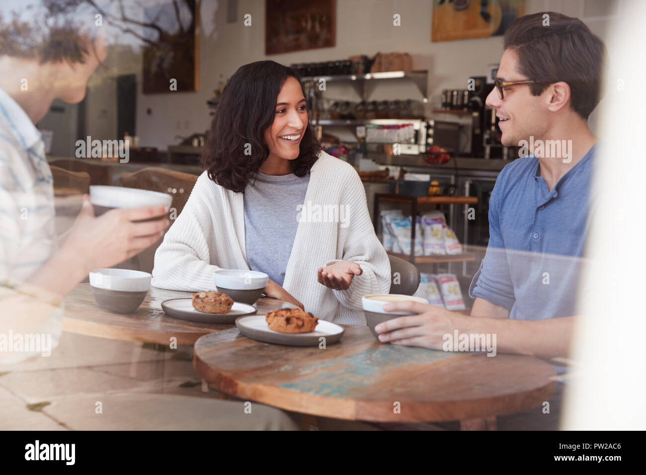Three happy young adult friends sit talking at a coffee shop Stock Photo
