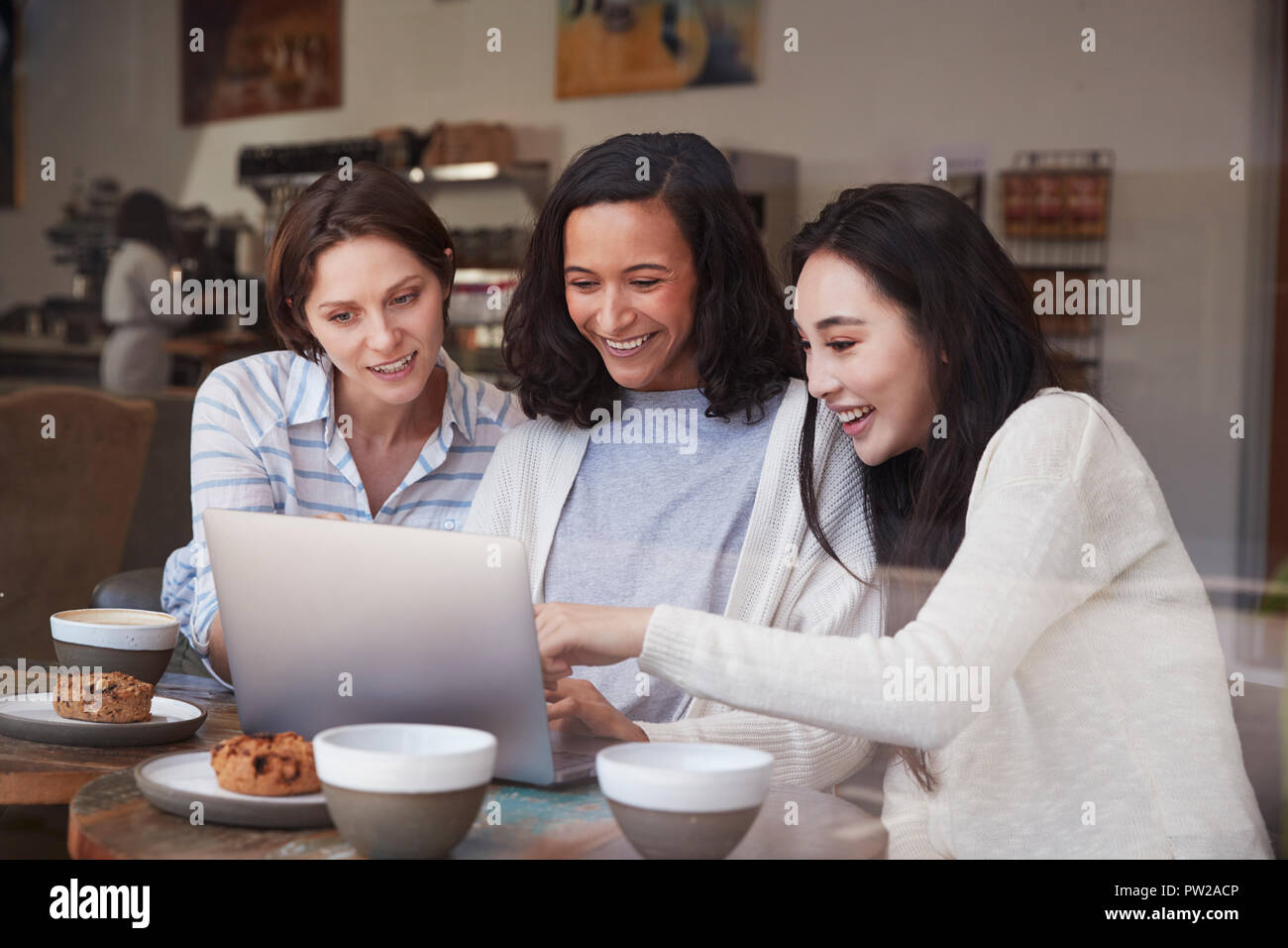 Female friends looking at a laptop together at a coffee shop Stock Photo