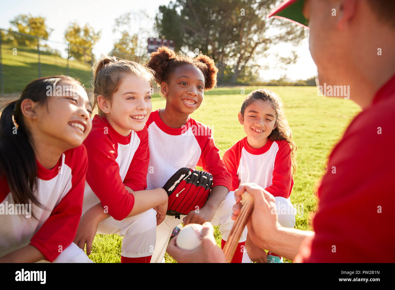 Girl baseball team in a team huddle with coach, listening Stock Photo