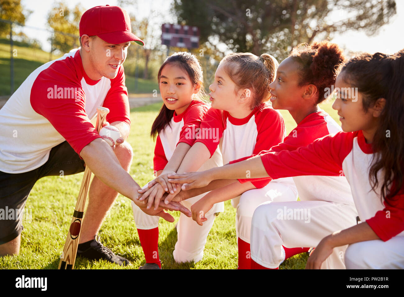 Girl baseball team kneeling with their coach, touching hands Stock