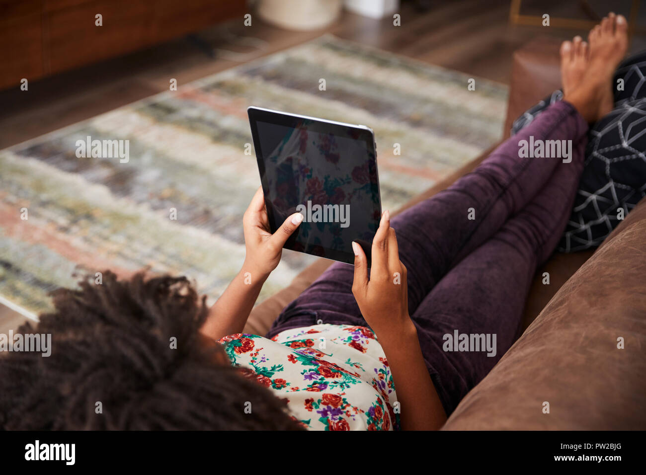Woman Lying On Sofa At Home Using Digital Tablet Stock Photo