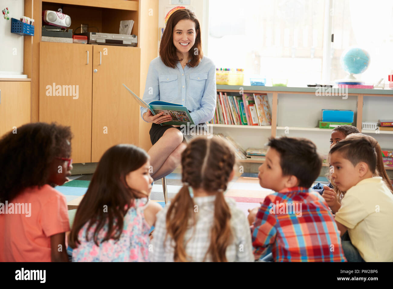 School kids sitting on floor in front of teacher, close up Stock Photo