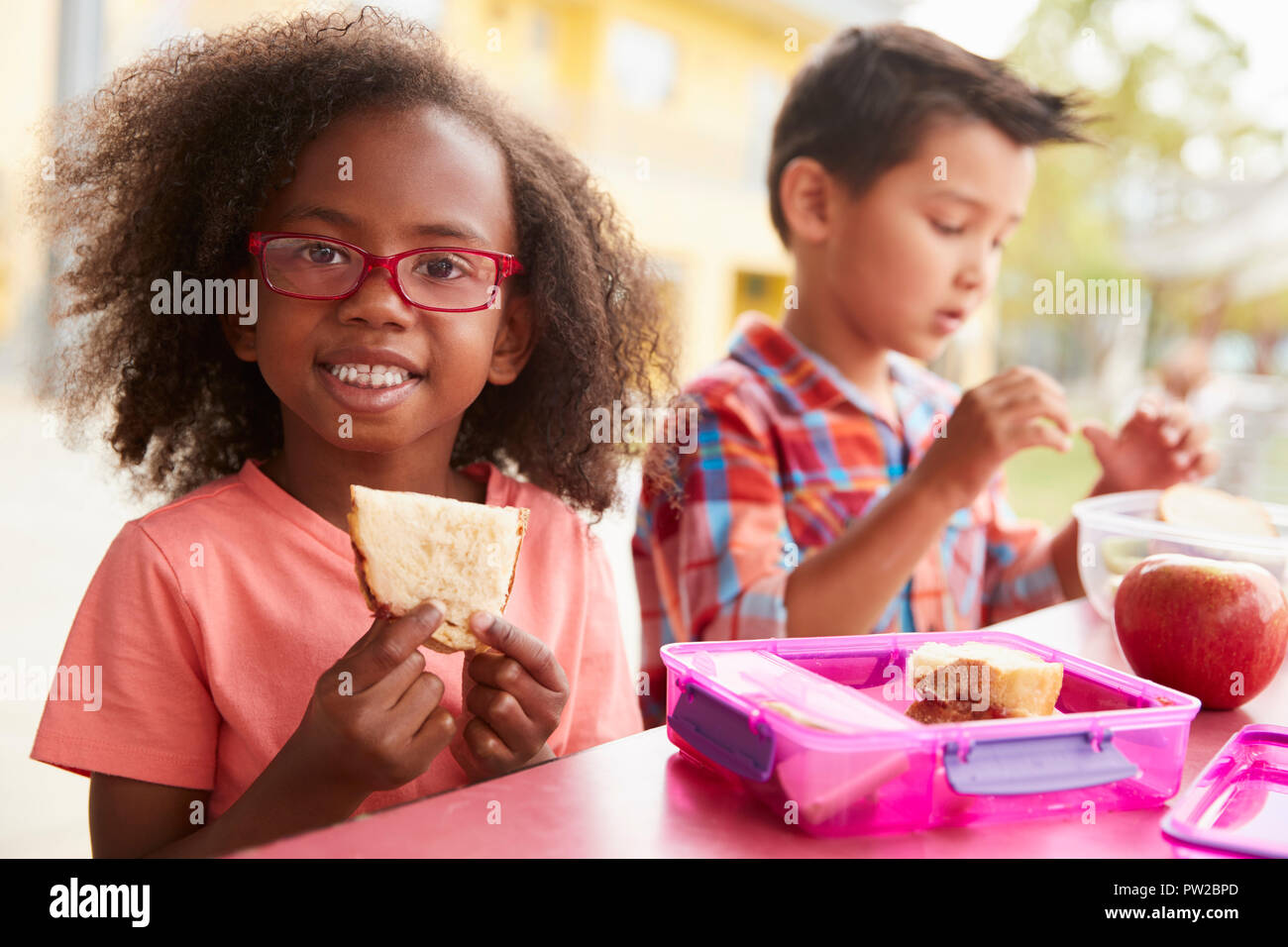 Young school girl and boy with packed lunches look to camera Stock