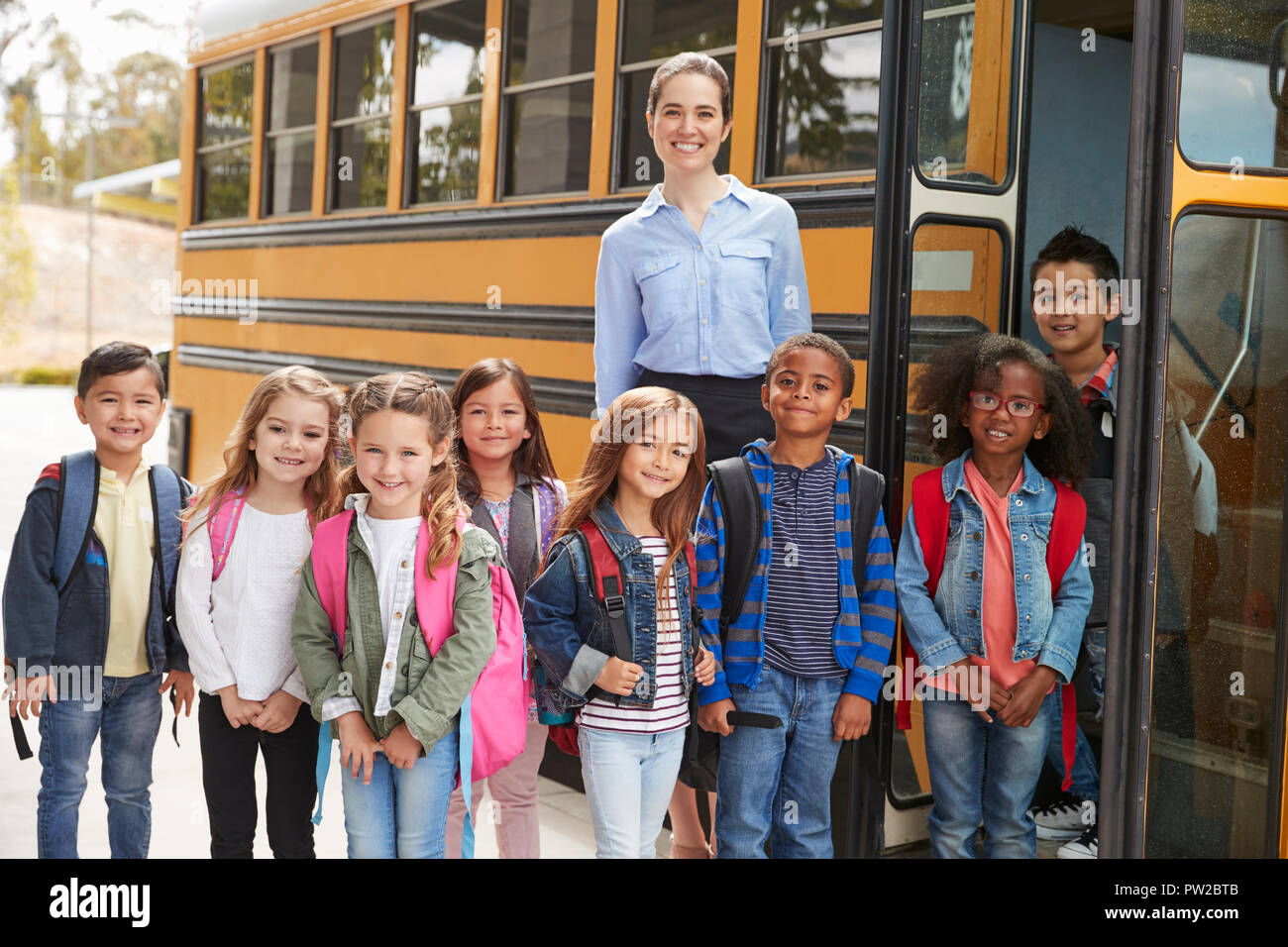 Elementary school teacher and pupils standing by school bus Stock Photo