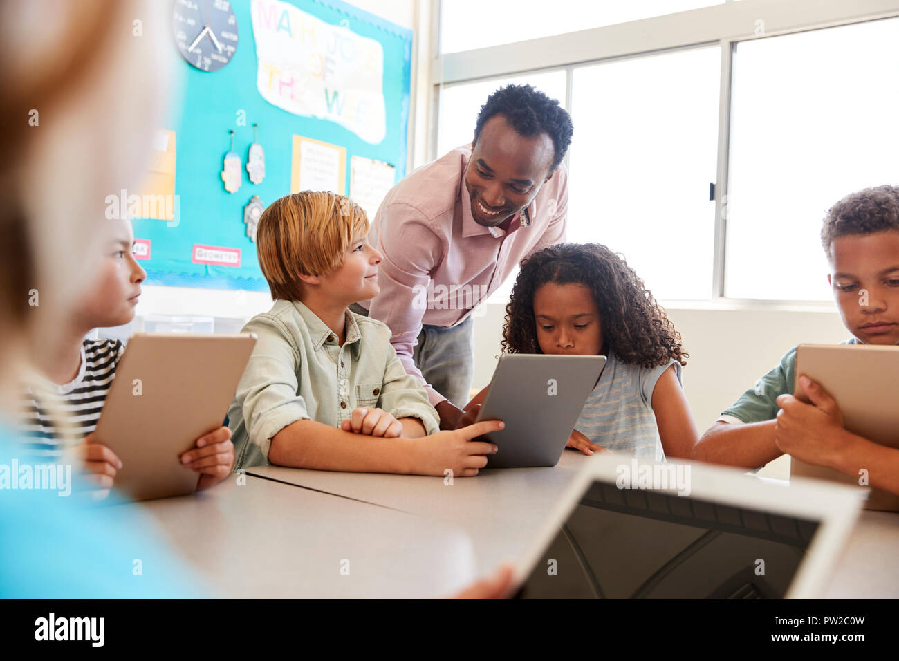 Teacher among kids with computers in elementary school class Stock