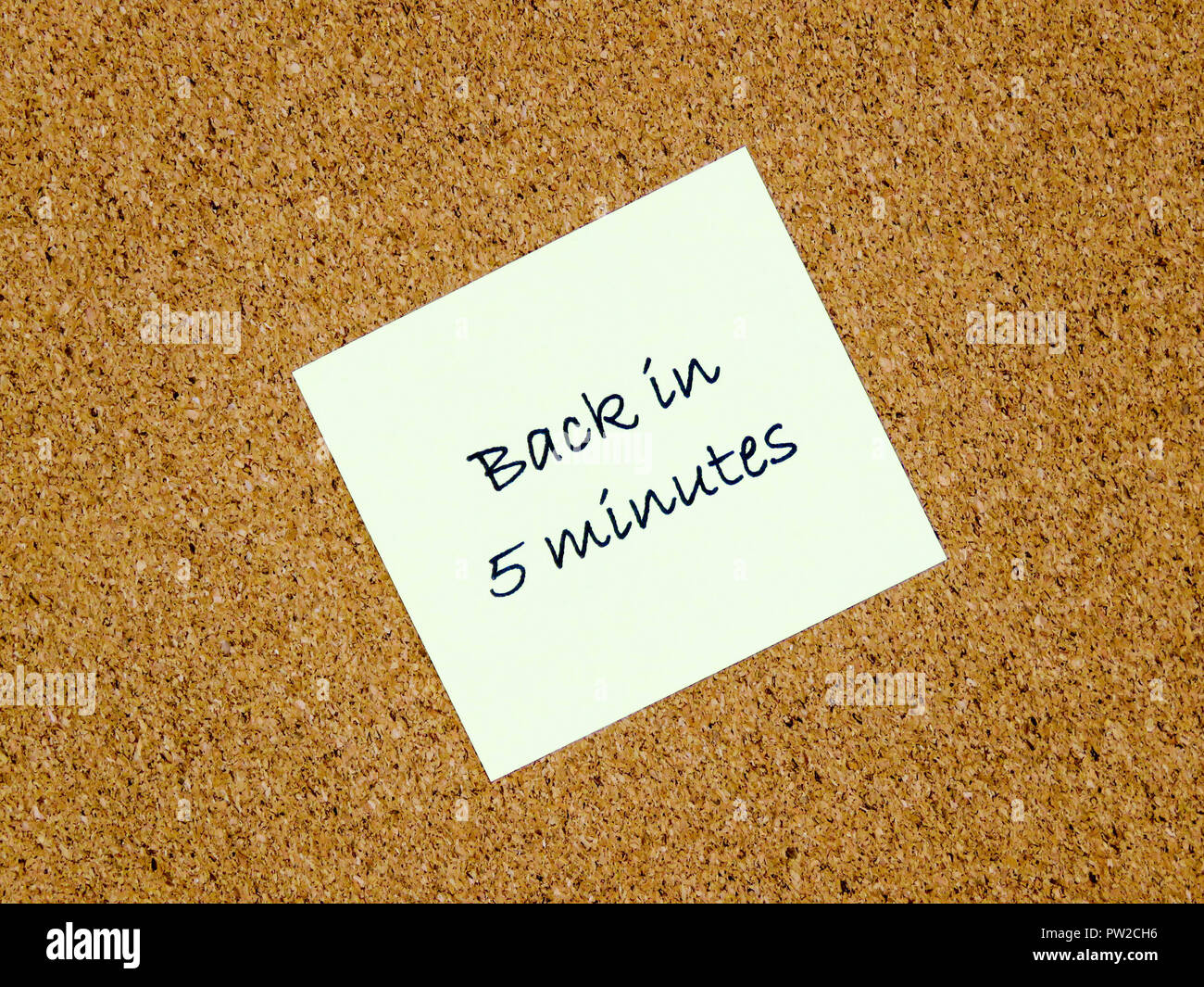 A yellow sticky note with back in 5 minutes written on it on a cork board background Stock Photo