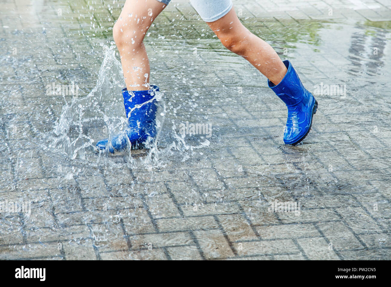 girl in blue rubber boots jumping in a puddle after a rain outdoor on