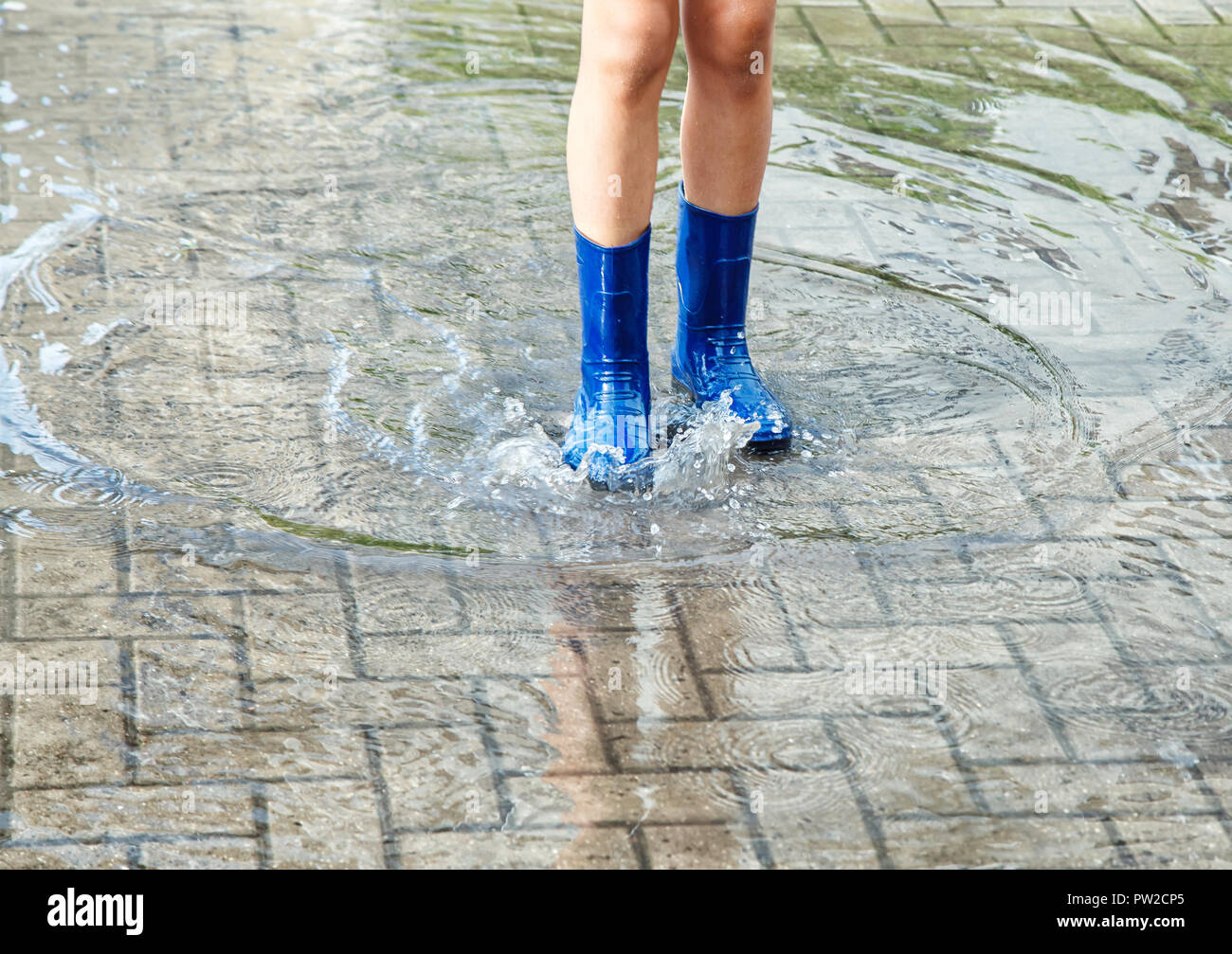 girl in blue rubber boots standing in a puddle after a rain outdoor on ...